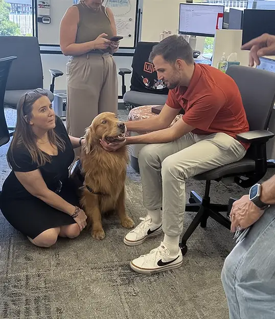 Therapy dog visiting a corporate office as employees engage during a workplace wellness event promoting stress relief and team morale